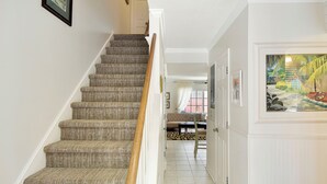 Una escalera con peldaños alfombrados y barandilla de madera, que conduce a una habitación con vistas a un paisaje tropical a través de un ventanal.