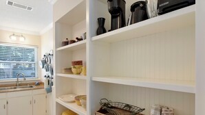 Cocina con armarios blancos, un fregadero y varios utensilios de cocina en estantes.