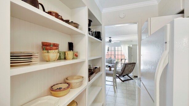 Una cocina con armarios blancos, un refrigerador y estantes con vajilla y utensilios de cocina.