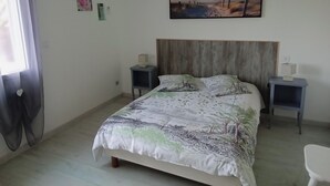 Une chambre à coucher comprenant un lit, deux tables de chevet, un climatiseur fixé au mur, une fenêtre avec des rideaux et un tableau sur le thème de la plage accroché au mur.