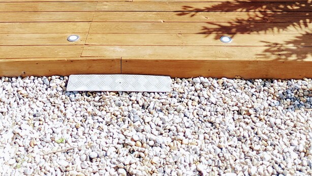 Une terrasse en bois avec une porte blanche, une fenêtre agrémentée d’une jardinière et un vélo.