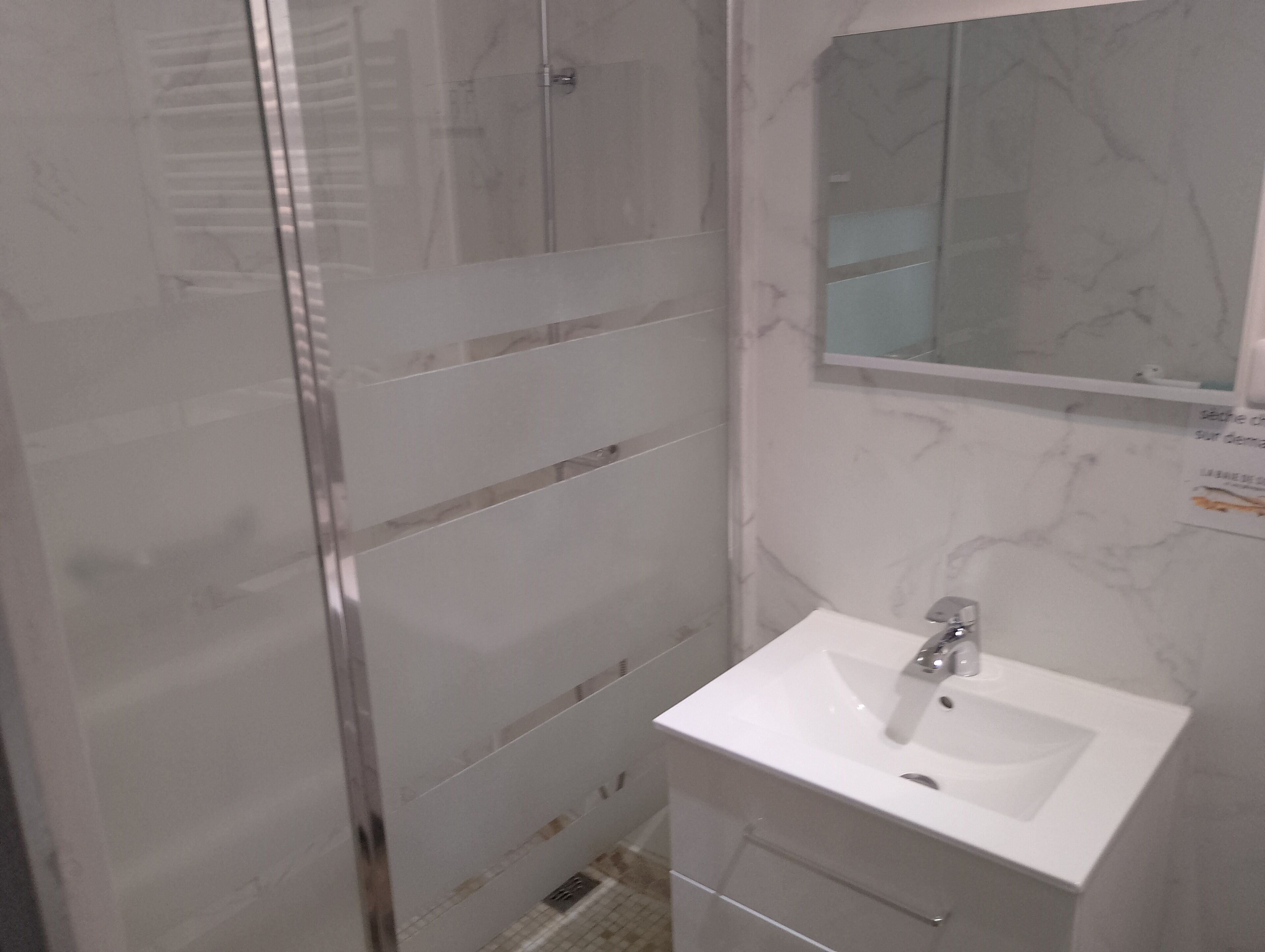 Ein Badezimmer mit Duschkabine aus Glas, einem weißen Waschbecken und einem Spiegel darüber.