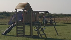 Un terrain de jeux avec un toboggan et des balançoires, situé dans un champ d’herbe.