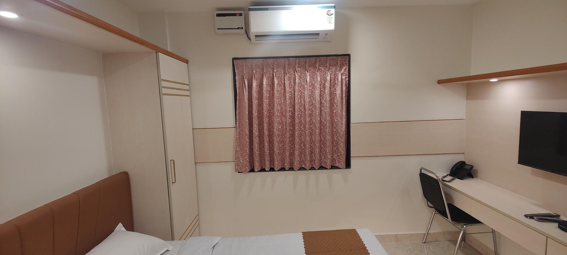 Un dormitorio con cama, escritorio, silla, aire acondicionado y televisor.