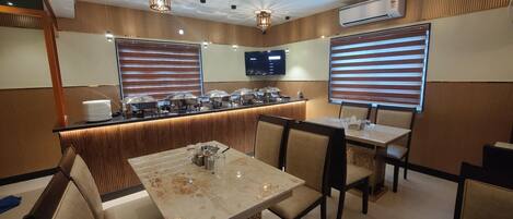Um restaurante com serviço de buffet, uma televisão na parede e uma área de estar com mesas e cadeiras.