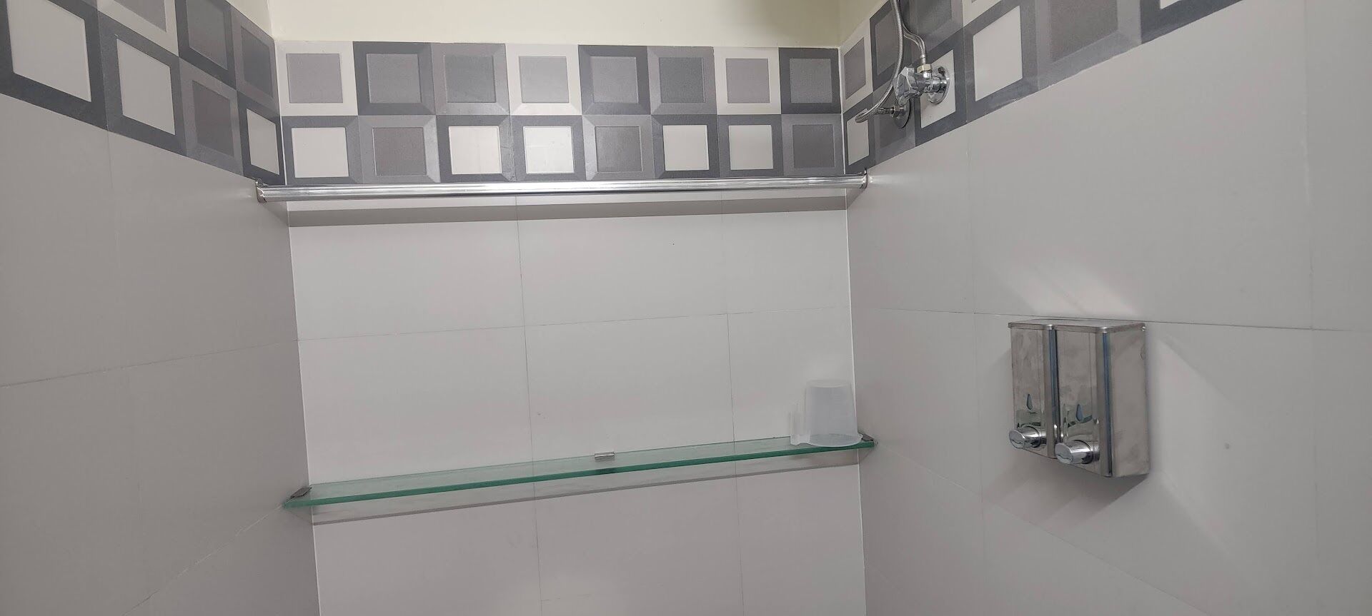 Un espace douche doté d’une étagère en verre et d’un distributeur de savon fixé au mur.
