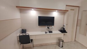 Una camera d'albergo con una scrivania, una televisione a schermo piatto, un telefono e un cestino.