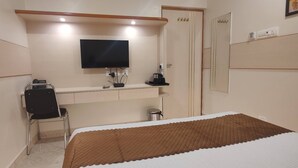 Una camera d'albergo con un letto, una scrivania con sedia, una televisione e un armadio.