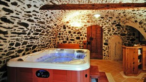Een kamer met stenen muren, een houten jacuzzi, een houten deur en een klein houten kastje.