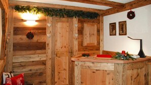 Een rustiek houten interieur met een houten bank, een kleine tafel met een rode kaars, en een muur met twee ingelijste foto's.