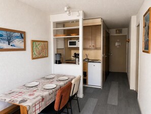 A compact kitchen with a microwave, sink, and cabinets. A dining table with chairs is set up in the foreground.