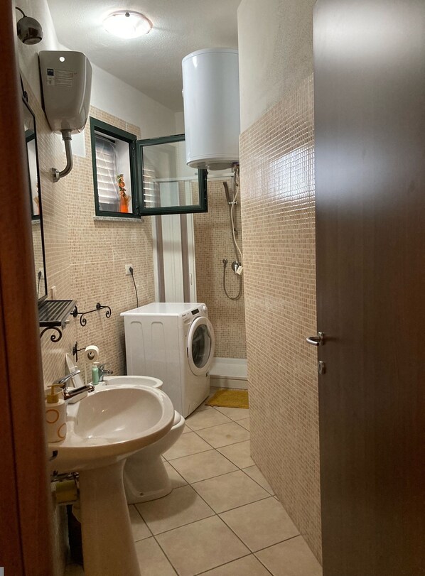 A compact bathroom with a sink, toilet, washing machine, and a shower area. - Sardinia RE - Borgo Marconi (Badesi)