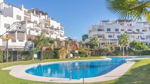 Una piscina rodeada de un césped cuidado, con edificios blancos al fondo.