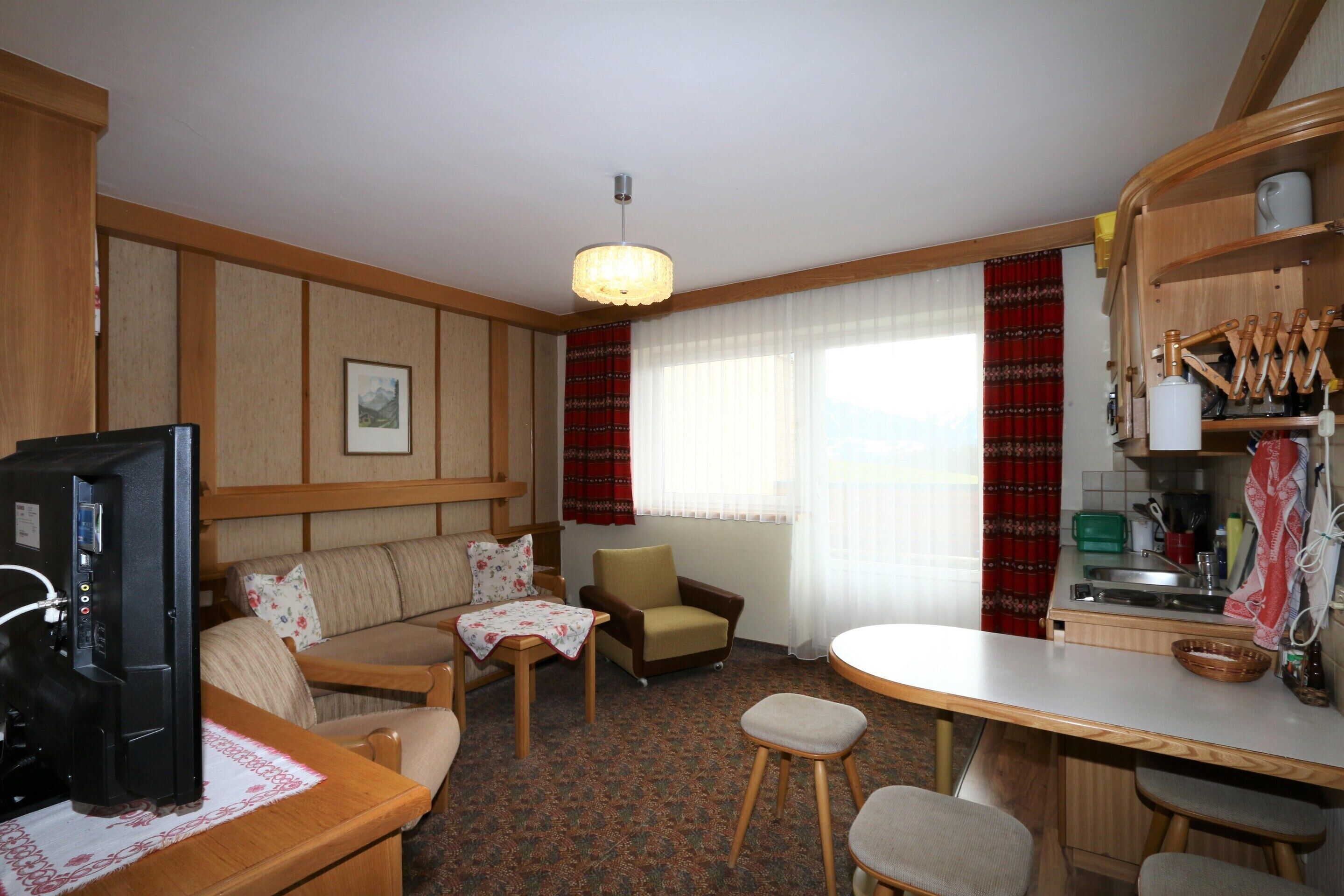 A compact living space with a kitchenette, a sofa, a chair, a small dining table, and a television.