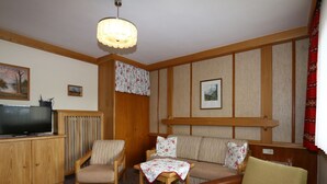 A cozy living room with a television, wooden furniture, a patterned sofa, and a table with a floral tablecloth. - Apartment in Vorberg Near Dachstein Glacier (Ramsau am Dachstein)