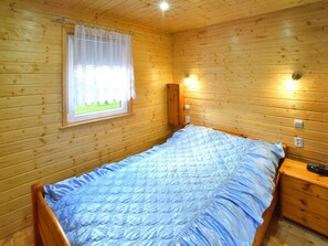 Una stanza con rivestimento in legno, un letto, una finestra con tenda, un comodino e un lampadario a parete.