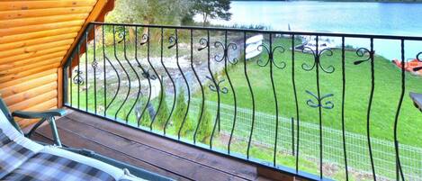A wooden deck with a metal railing overlooking a grassy area and a body of water.
