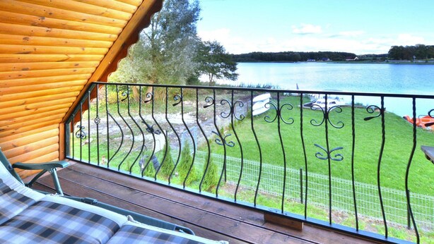 A wooden deck with a metal railing overlooking a lake, a grassy area, and a boat. - Cottage by Lake Ostrowieckie With Private Beach (Malechowo)