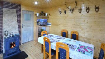 A wooden interior with a fireplace, a dining table with chairs, a television, and antler decorations on the wall.