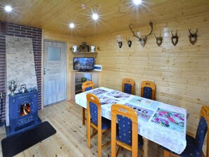A wooden interior with a fireplace, a dining table with chairs, a television, and antler decorations on the wall. - Large Holiday Home With a Lake View (Malechowo)
