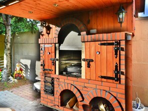 A brick-built outdoor oven with a chimney, a wooden roof, and a metal door. - Large Holiday Home With a Lake View (Malechowo)