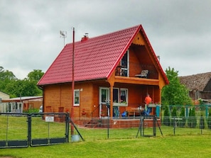 Ein hölzernes Haus mit rotem Dach, einem Balkon und einem umzäunten Hof.