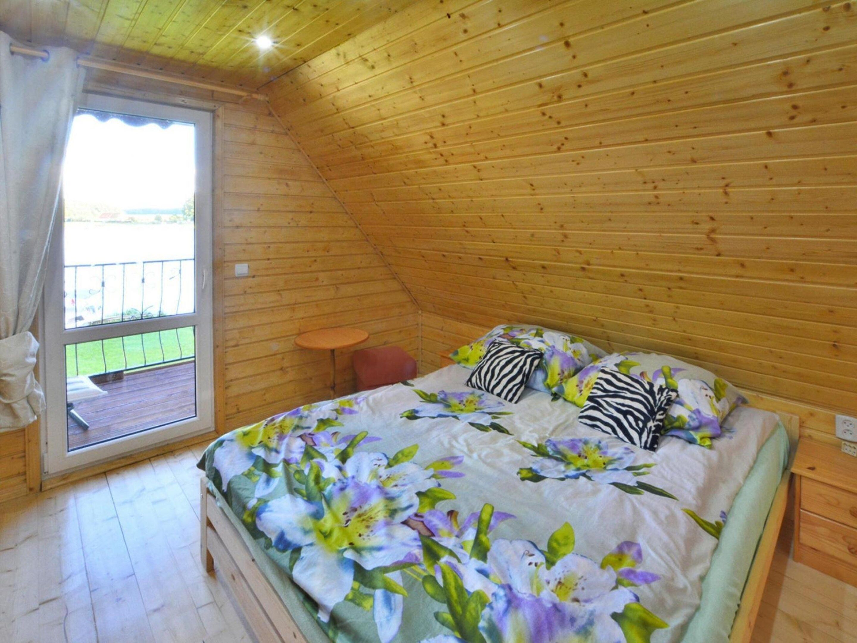 A bedroom with a sloped ceiling, a bed with floral bedding, a small round table, and a view through a window.
