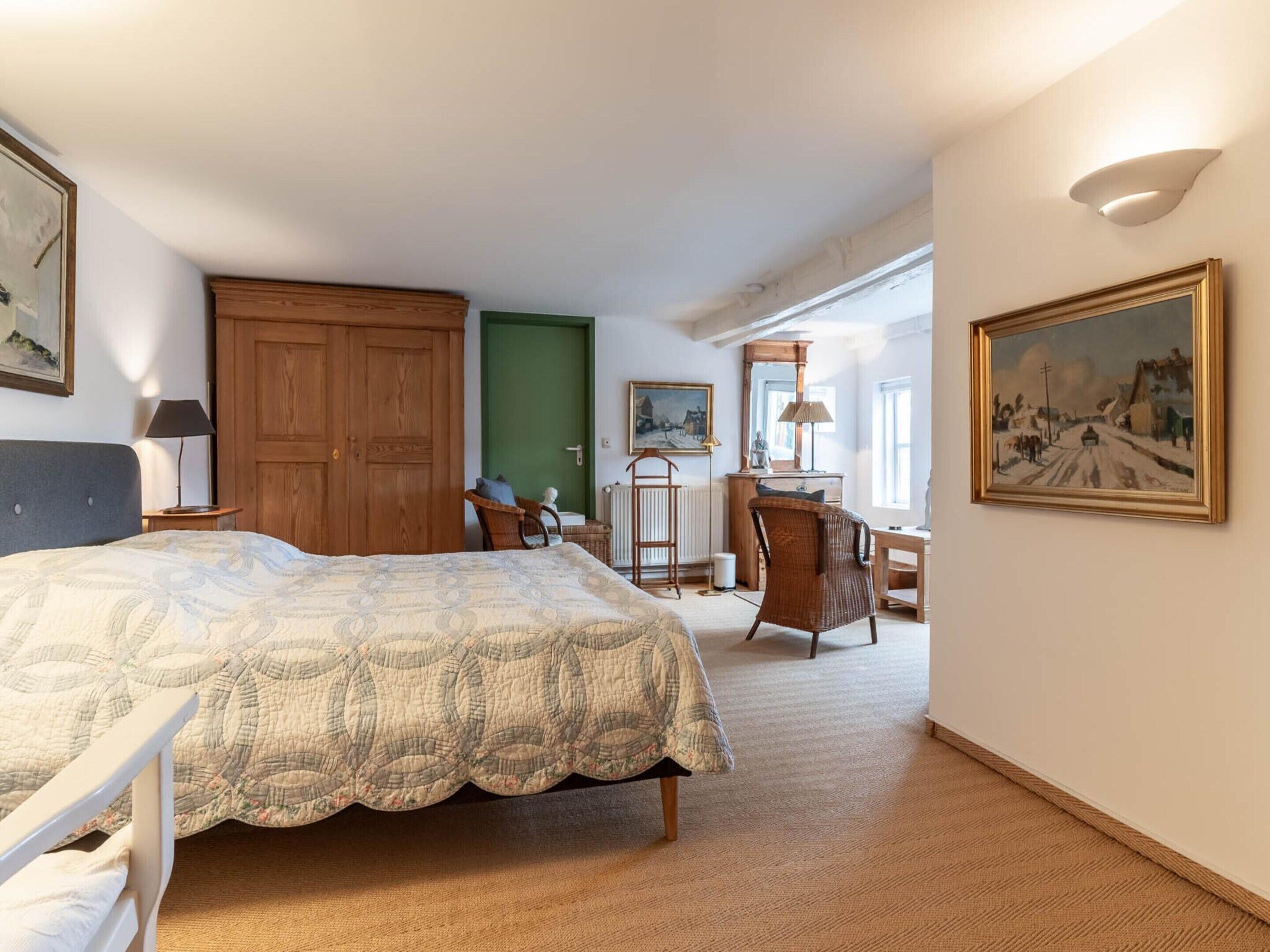 A bedroom with a bed, a desk, a chair, a wardrobe, and a painting on the wall.