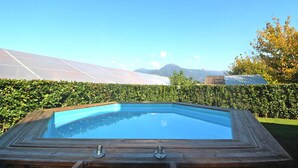 A rectangular swimming pool with a wooden frame, surrounded by a well-maintained hedge, set against a backdrop of mountains and clear skies. - Holiday Home Fragola, Capezzano Pianore (Camaiore)