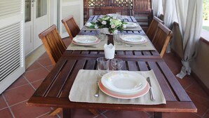 A wooden dining table set for four with floral centerpieces, chairs, and a view of a wooden fence and greenery. - Holiday Home Fragola, Capezzano Pianore (Camaiore)