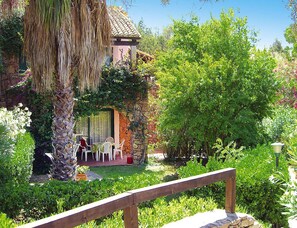 A garden with a stone building, a palm tree, and a wooden fence. - Apartment in Sardinian Style With Pool (Olbia)