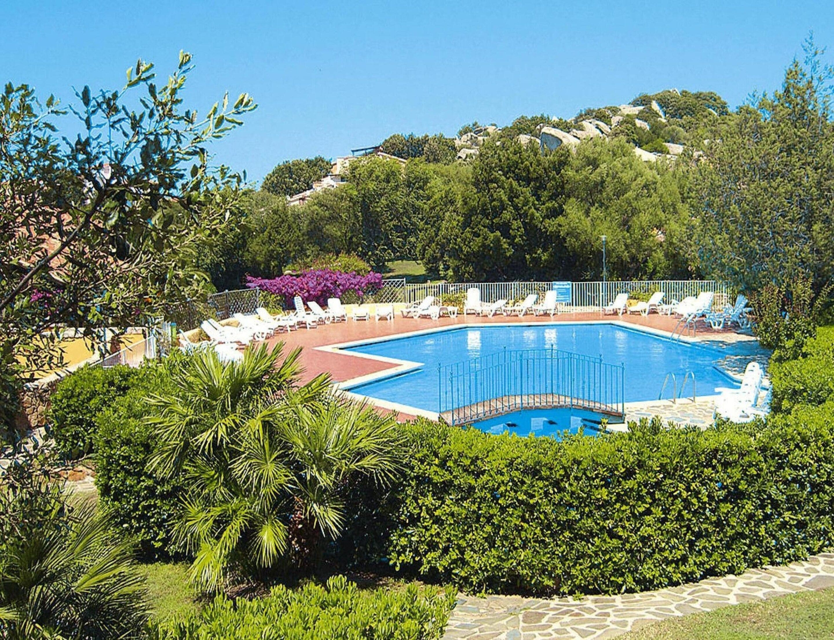 Piscina rodeada por espreguiçadeiras e vegetação.