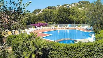 Piscina rodeada por espreguiçadeiras e vegetação.