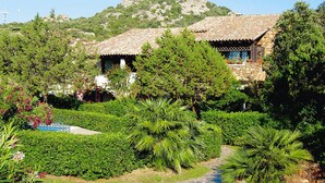 A traditional stone building with a tiled roof, surrounded by lush greenery and a clear sky. - Apartment in Sardinian Style With Pool (Olbia)