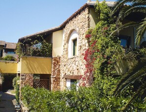 A stone building with a yellow facade, a balcony with climbing plants, and a clear blue sky. - Apartment in Sardinian Style With Pool (Olbia)
