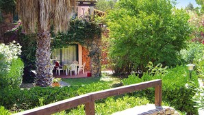 A stone building with a tiled roof, surrounded by lush greenery and a wooden deck with chairs. - Apartment in Sardinian Style With Pool (Olbia)