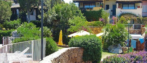 Un patio con muros de piedra, cerca metálica y diversas plantas y flores.