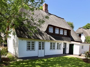 Une maison de campagne traditionnelle, avec des murs blancs, un toit de chaume, un petit porche et une pelouse bien entretenue.