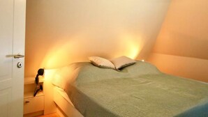 A bedroom with a bed, pillows, a bedside lamp, and a hanging light fixture. - Wohnung fur 4 Personen mit Garten in Nieblum (Nieblum)