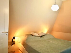 Een slaapkamer met een bed, kussens, een bedlampje en een hangende lamp.