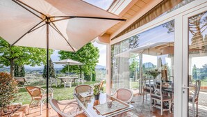 A patio with a glass table and chairs, surrounded by a large umbrella, overlooking a scenic landscape. - Casa Paradiso With Wonderful Panorama (Capannori)