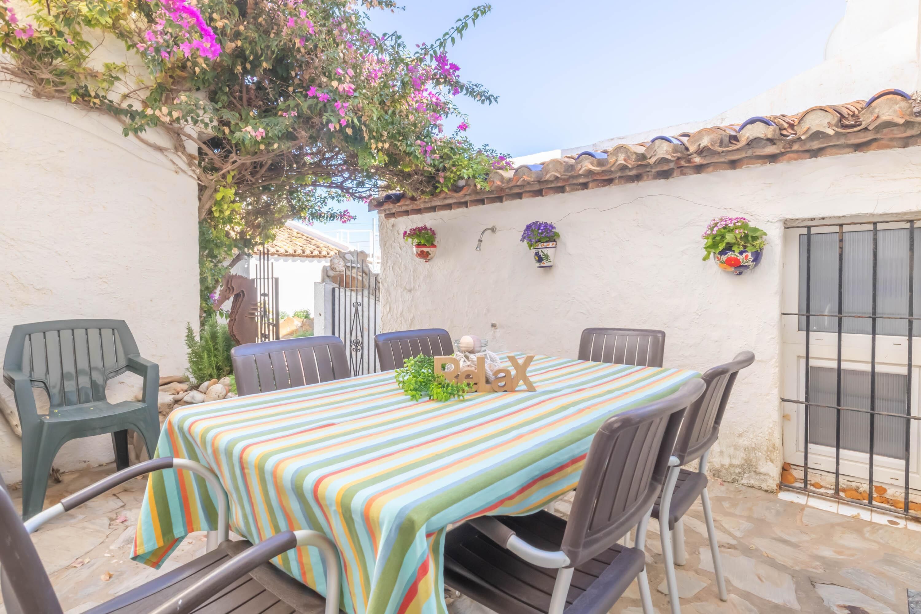 A patio with a striped tablecloth, metal chairs, and hanging flower pots.