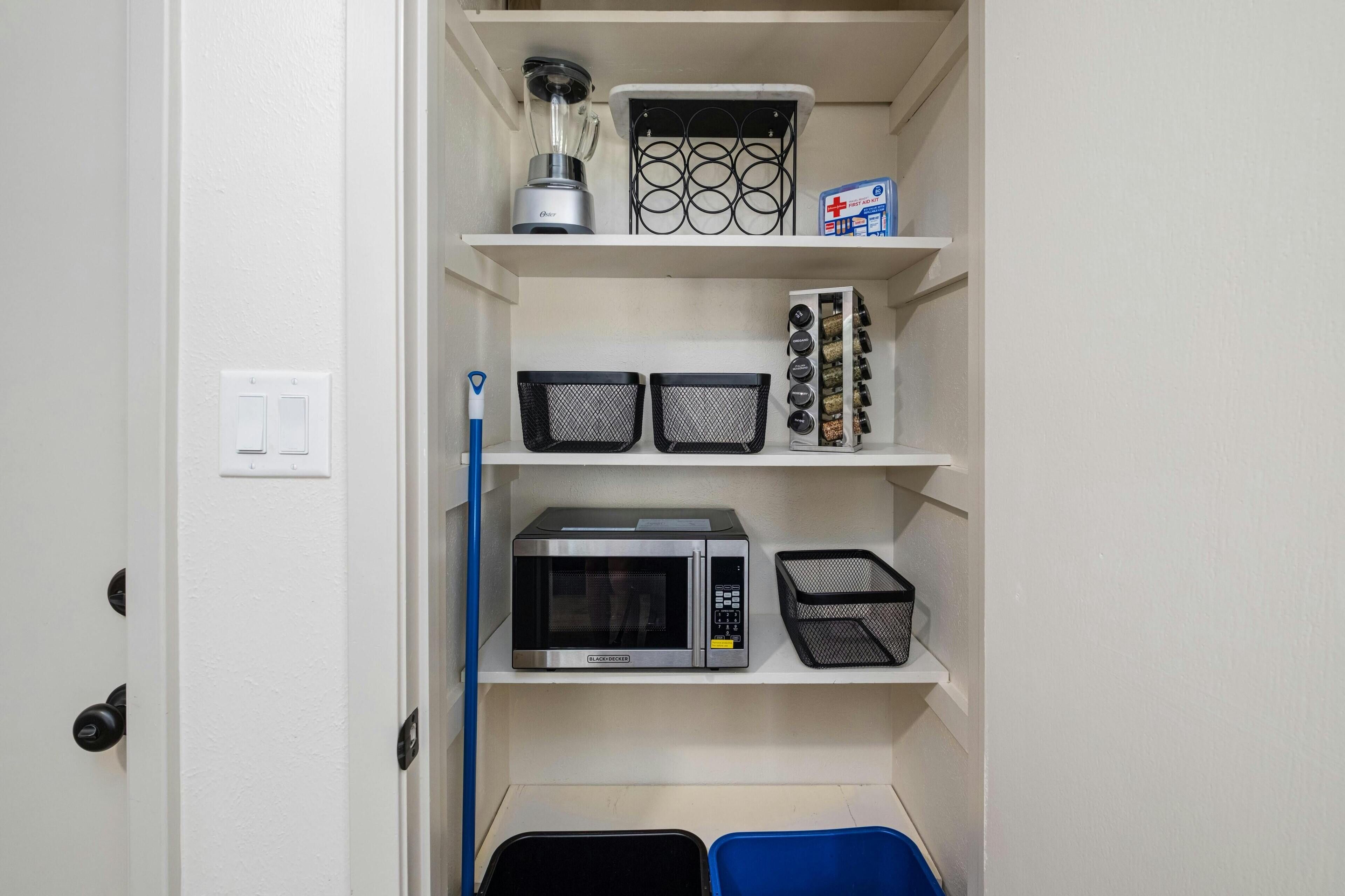 A compact kitchen with a microwave, blender, and storage baskets on shelves.