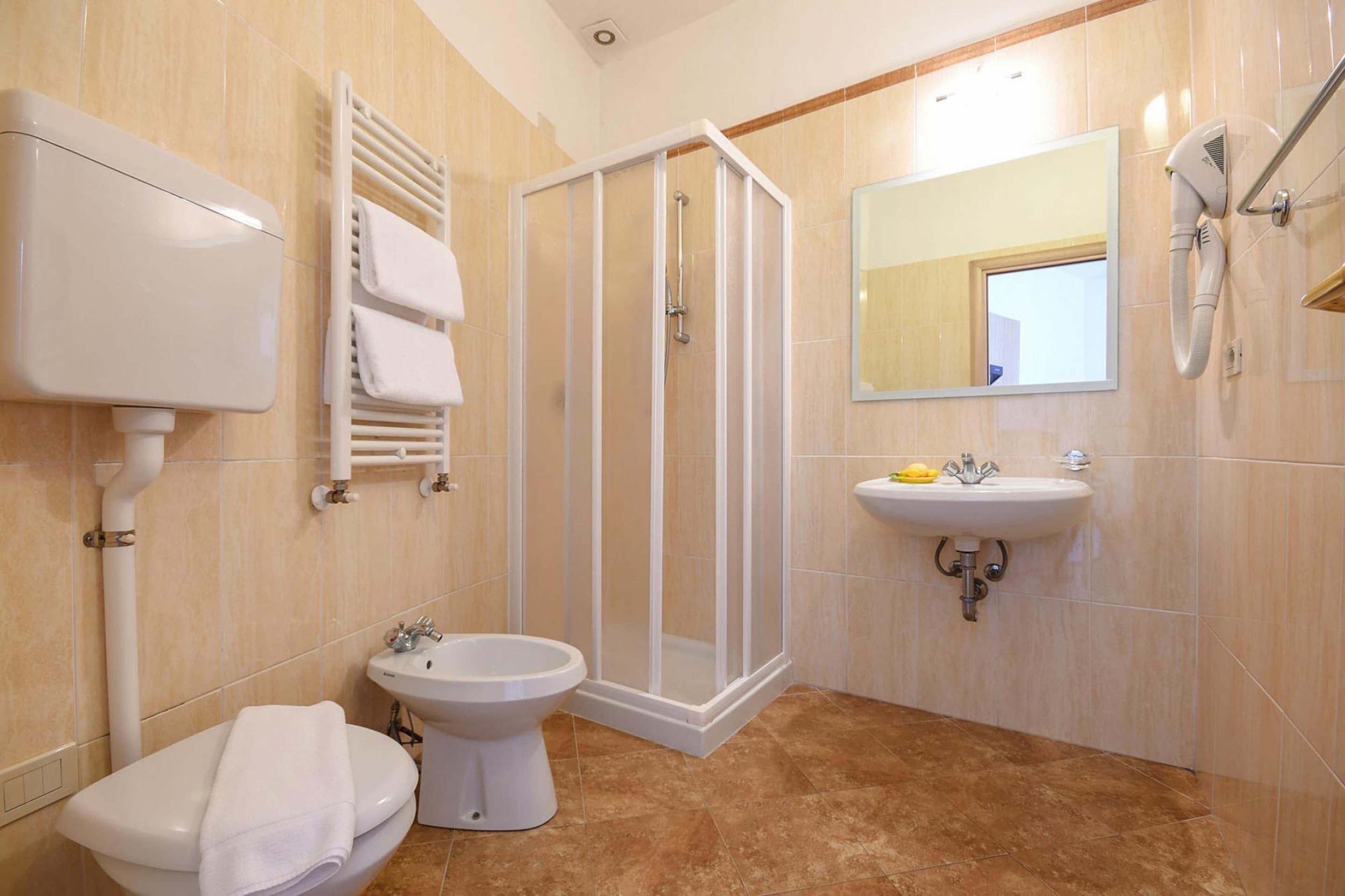 A bathroom with a toilet, bidet, shower, sink, and towel rack.