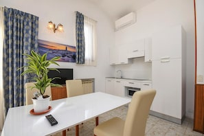 A modern kitchen with white cabinets, a built-in oven, and a small dining area with a white table and chairs. - Apartment in Limone With Balcony or Terrace (Limone sul Garda)