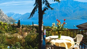 Ein Tisch mit Blumen am Balkon mit Blick auf eine Berglandschaft und ein Gewässer.