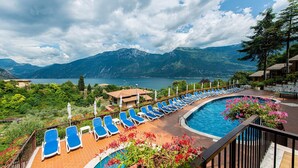 Ein Poolbereich mit Liegestühlen, einem Schwimmbecken und einer Berglandschaft im Hintergrund.