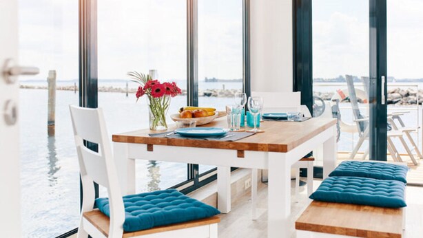 A modern dining area with a wooden table, white chairs, and blue cushions. - Houseboat in Egernsund at the Marina Minde (Broager)