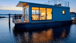 A modern houseboat with a glass exterior, a deck area, and a kitchen visible inside. - Houseboat in Egernsund at the Marina Minde (Broager)