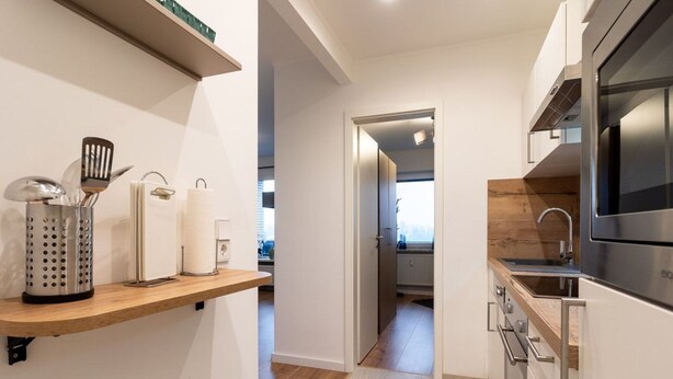 A modern kitchen with a wooden countertop, stainless steel appliances, and a view into the adjacent room. - Ferienwohnung mit Balkon in Westerdeichstrich (Westerdeichstrich)